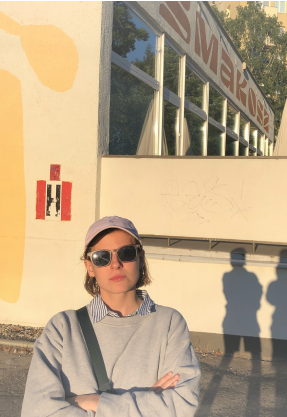 Fashionable woman in sunglasses and hat stands confidently in front of a building