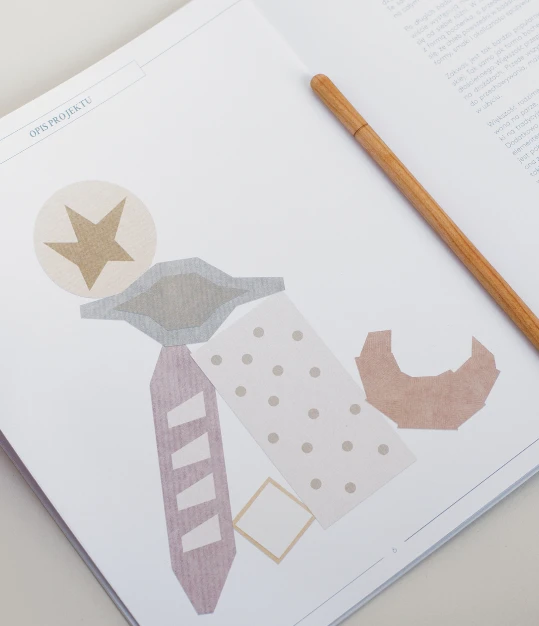 Open page of the publication with a paper-collage illustration of bread shapes, a wooden pen resting on top