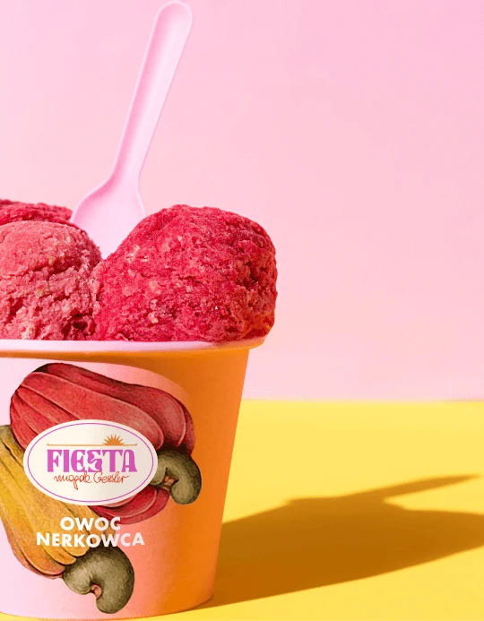 Close-up of raspberry-red Fiesta sorbet scoops in an orange cup labelled "owoc nerkowca", with a pink spoon on a pink and yellow backdrop
