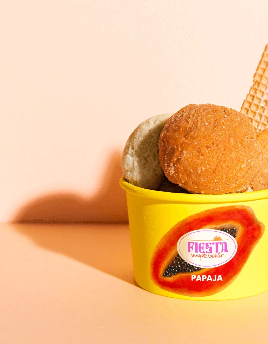 Yellow Fiesta papaja cup with two scoops of ice cream and a wafer against a peach background